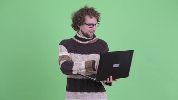 Happy Young Bearded Man Thinking While Using Laptop