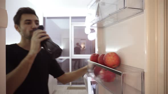 Healthy Eating Food and Diet Concept Dark Haired Young Man Opening Fridge at Home Kitchen Drinking