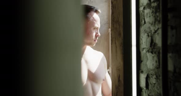 Athlete With Naked Torso Standing By The Window, Looking At The Camera