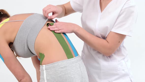 Physiotherapist sticks kinesio tapes to the small of the back of female patient, kinesiology taping