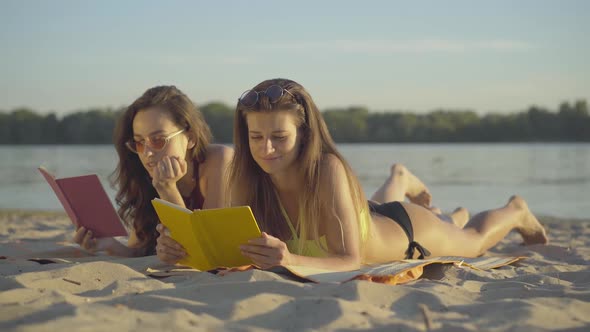 Portrait of Absorbed Young Caucasian Women Reading on Sandy Beach at Summer Resort. Beautiful