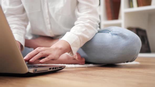 Woman Uses Laptop While Sitting On  Living Floor Of Apartment. Girl Makes Purchases On Internet