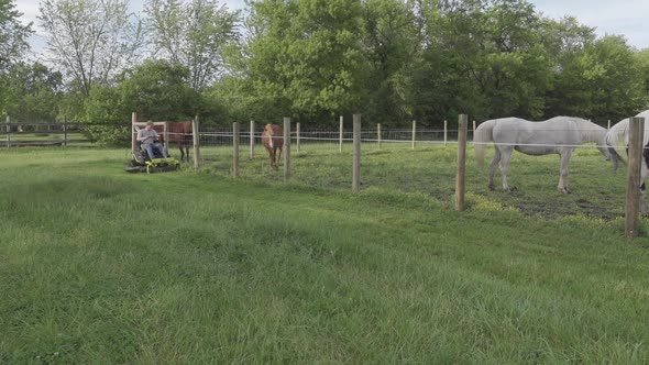 Man Trimming The Grass Using An Electric Zero Turn Mower Near The Pasture Land For Horses. wide shot