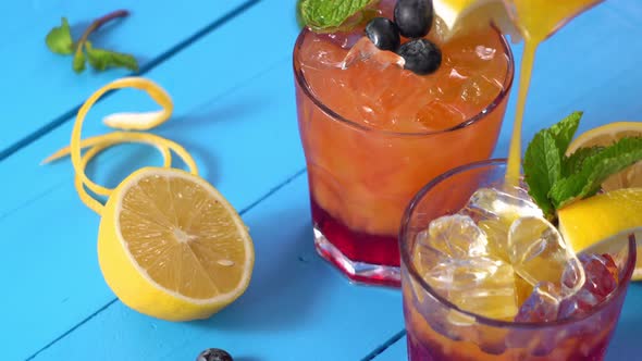 Orange juice being poured into red cocktail drink on wooden blue table