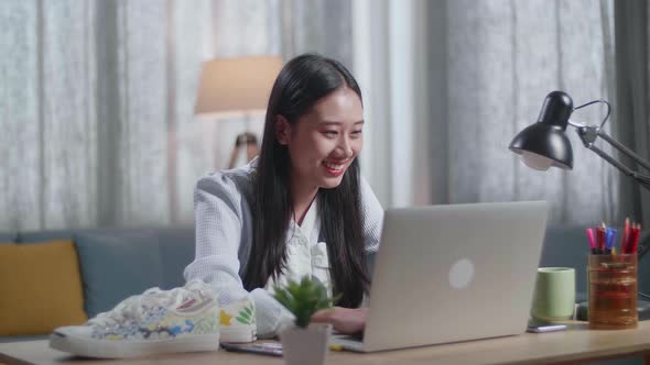 Smiling Asian Female Footwear Going Through The Room, Sits Down And Starts Working At Her Laptop