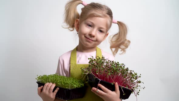 A Small Blonde Girl Smiles and Holds a Seedling of Micro Greens in Her Hands