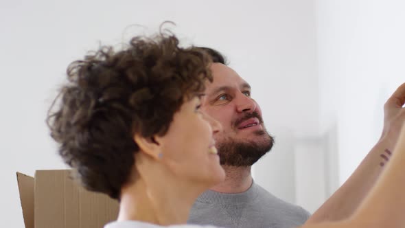 Loving Husband Watching his Wife Hang Picture Up on Wall