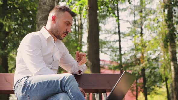 Business Man in a White Shirt Working Online with a Laptop on a Bench