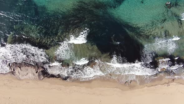 Top Aerial View of Sandy Coast with Foamy Transparent Waves Rolling In. Camera Moves Up From