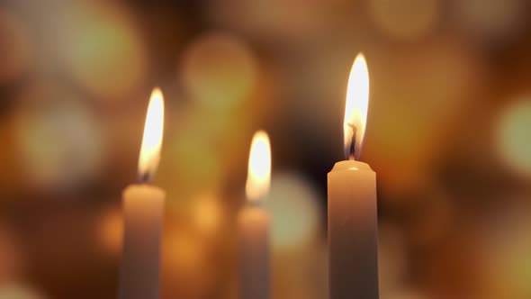 Footage of Burning a Three Candles on on a Yellow Background of Colored Blurred Bokeh