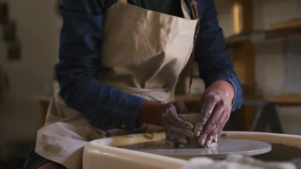 Mid section of female potter creating pottery on potters wheel at pottery studio