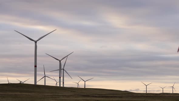 Motion the Blades of a Large Wind Turbine in a Field Against a Background of Orange Sunset on the