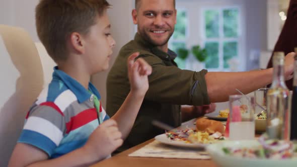 Smiling caucasian family at table serving each other food before meal