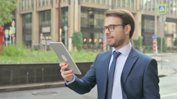 Businessman making Video Call on Tablet while Walking in Street