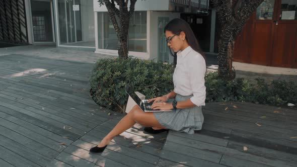 Asian Attractive Young Woman Wearing Glasses Working at Her Laptop at an Outdoor Terrace Cafe
