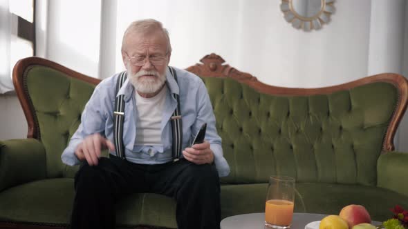 Old Fan, Grandfather with Glasses for Sight and Beard with Remote Control Very Emotionally Watches