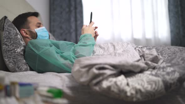 Coughing Man with Fever Using His Phone During Home Isolation. Quarantined Man with Protective