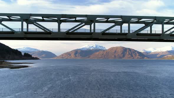 Flying Under a Large Iron Bridge and Beautiful Mountainous Landscape Reveal