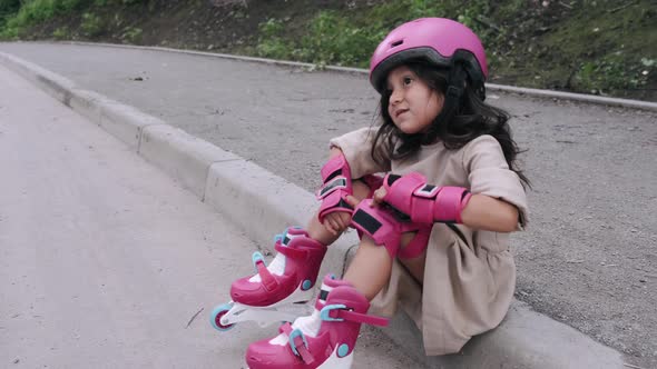 Little Girl in Helmet Is Putting Protective Equipment on Road