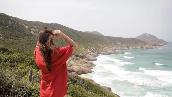 Young woman enjoying the sea breeze on her face and hair, many rocks on the sea slope in Praia Brava