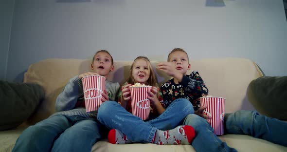 Group of Children Watching Movie on TV in the Evening at Home and Eat Popcorn