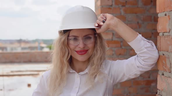 Female Architect in Business Attire and a White Helmet Stands at the Construction Site
