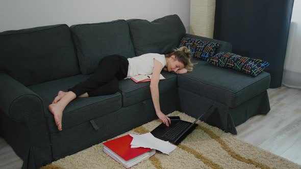 Young woman is lying on the bed at home and laptop is on the floor.