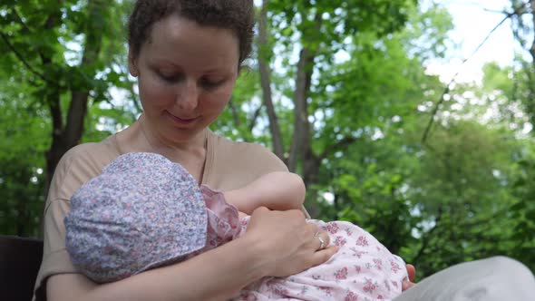 A Woman Is Breastfeeding Her Baby Outdoors.