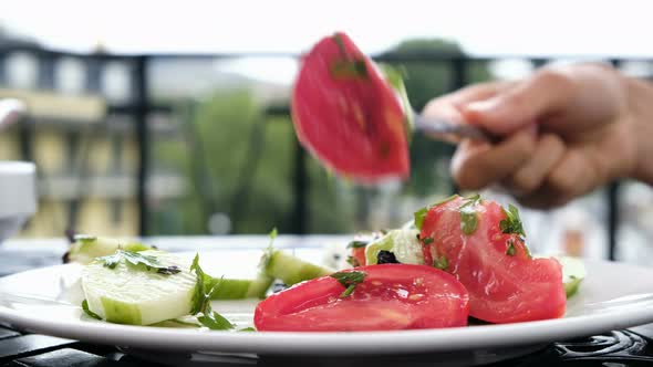 Woman in a Restaurant Eats Salad From Cucumbers and Tomatoes with a Fork Close-up