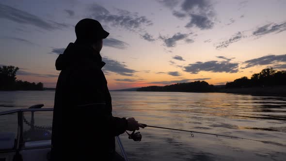 A Fisherman Casts a Spinning Rod From a Boat on the River