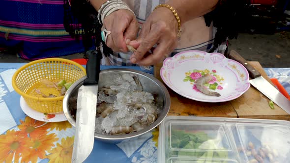 Old Hands Peeling and Preparing Shrimp (Prawns) at Open Air Kitchen, Additional Vegetables on Table