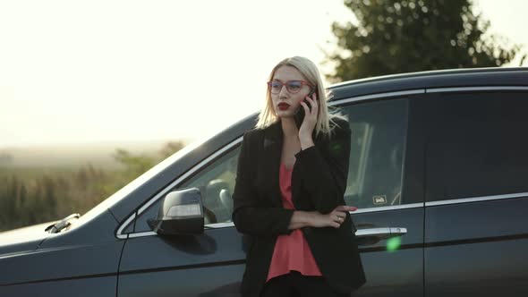 Pretty Blonde in Glasses Talking on the Phone Emotionally at Car Out of City