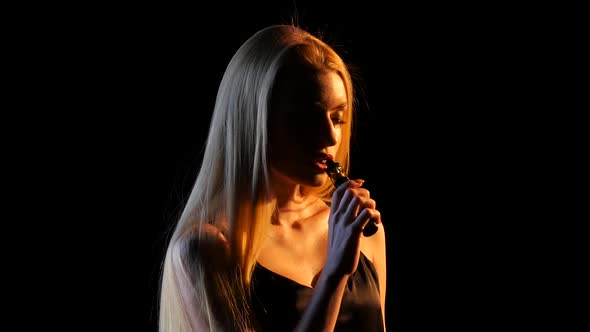 Blonde in a Spacious Room Smokes an Electronic Cigarette. Black Background