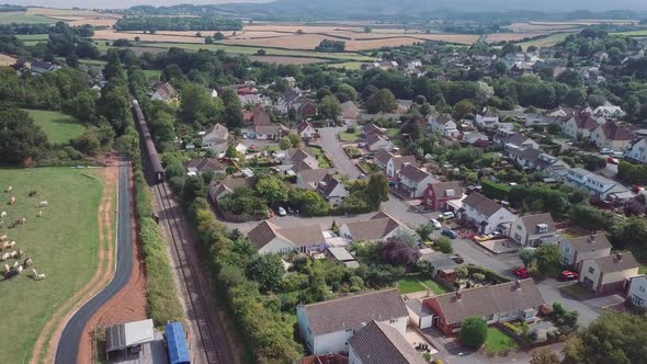 Stationary aerial wide shot of the village of Washford, Somerset with a diesel train heading east aw