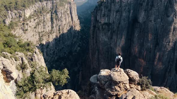 Traveler Guy with a Backpack Stands on a Cliff Overlooking Canyon