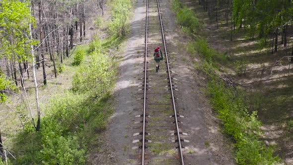 A Tourist with a Backpack Goes Along the Railway in a Forest Area