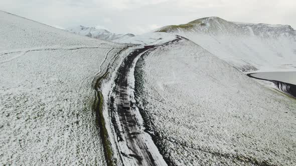 Aerial of a Car Driving on a Snow Covered Dirt Road in Highlands of Iceland