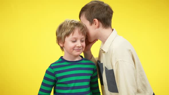 Positive Smiling Boys Sharing Secrets Whispering on Ear at Yellow Background