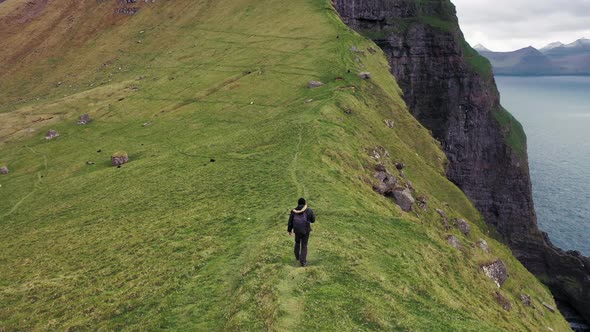 Hiker with a Backpack Walks Up Hill Along a Cliff on Kalsoy, Faroe Islands