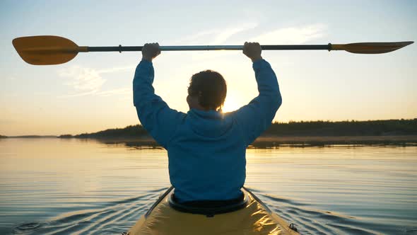 Outdoor Activities, Happy Man Raises Paddle Above Head Against the Background of Sunset Rays Sitting