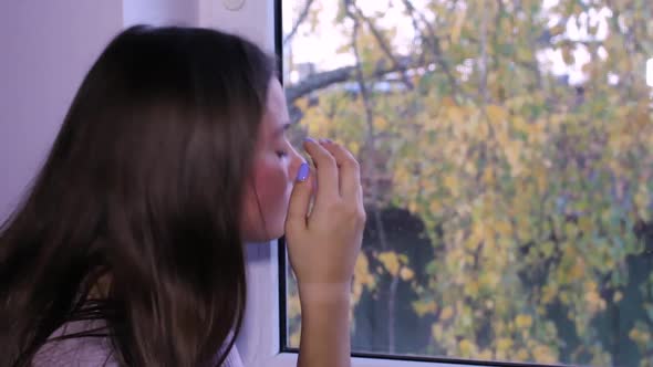 Beautiful teenage girl standing next to a window, daydreaming