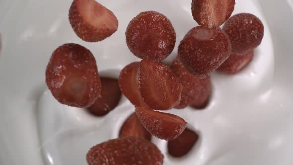 Sliced and whole fresh strawberries drop up onto yogurt - High-angle shot