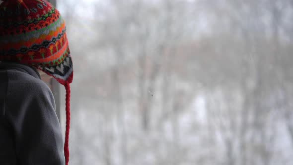 A Little Boy Looks Through the Window on a Heavy Snowfall Waiting for Christmas To Come. Slowmotion