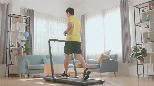 Back View Of Asian Man Running On A Treadmill At Home