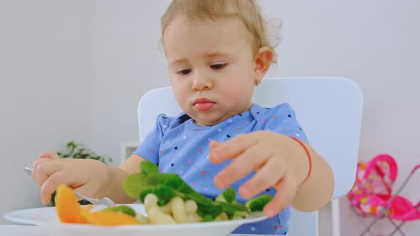 The Child Eats Pasta and Vegetables