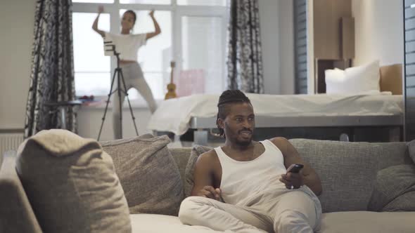 Relaxed African American Father Watching TV Home Blurred Cheerful Teenage Daughter Dancing