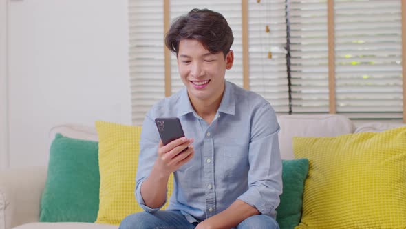 Millennial asian young man looking mobile phone laughing with good news or discount voucher