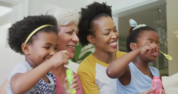 Happy african american grandmother with adult daughter and granddaughters blowing bubbles