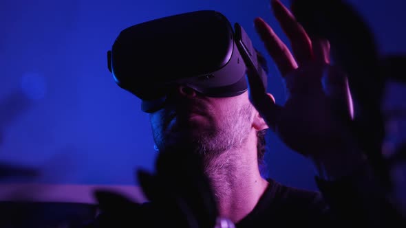 Close-up of a bearded man wearing VR glasses in a dark room with blue light