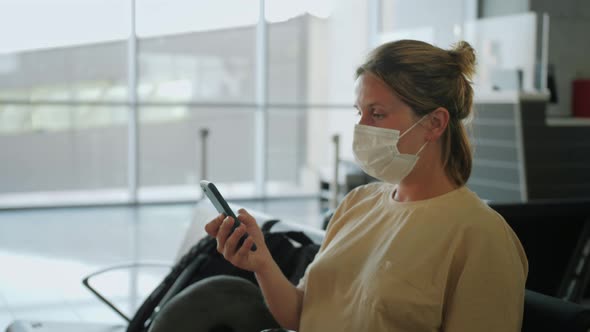 Woman Wearing Medical Mask Protection and Using Smartphone While Sitting in Airport Terminal and